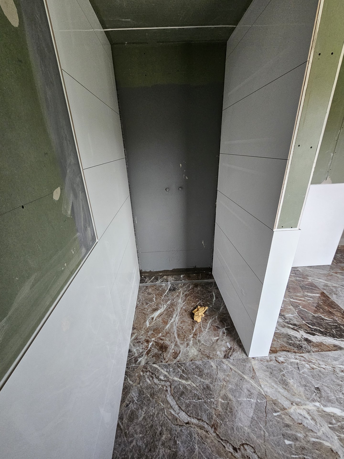 Grau beschichtete Abdichtung an der Rückwand einer Duschnische mit offengelegten Armaturanschlüssen in Harburg (Schwaben)